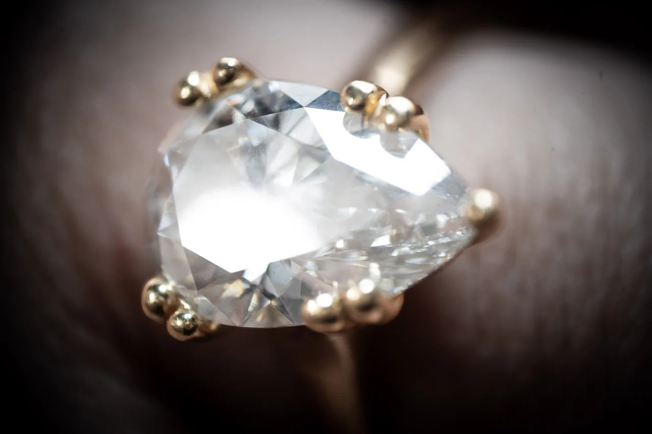 Extreme macro photograph of a clear faceted gemstone held in gold prongs.