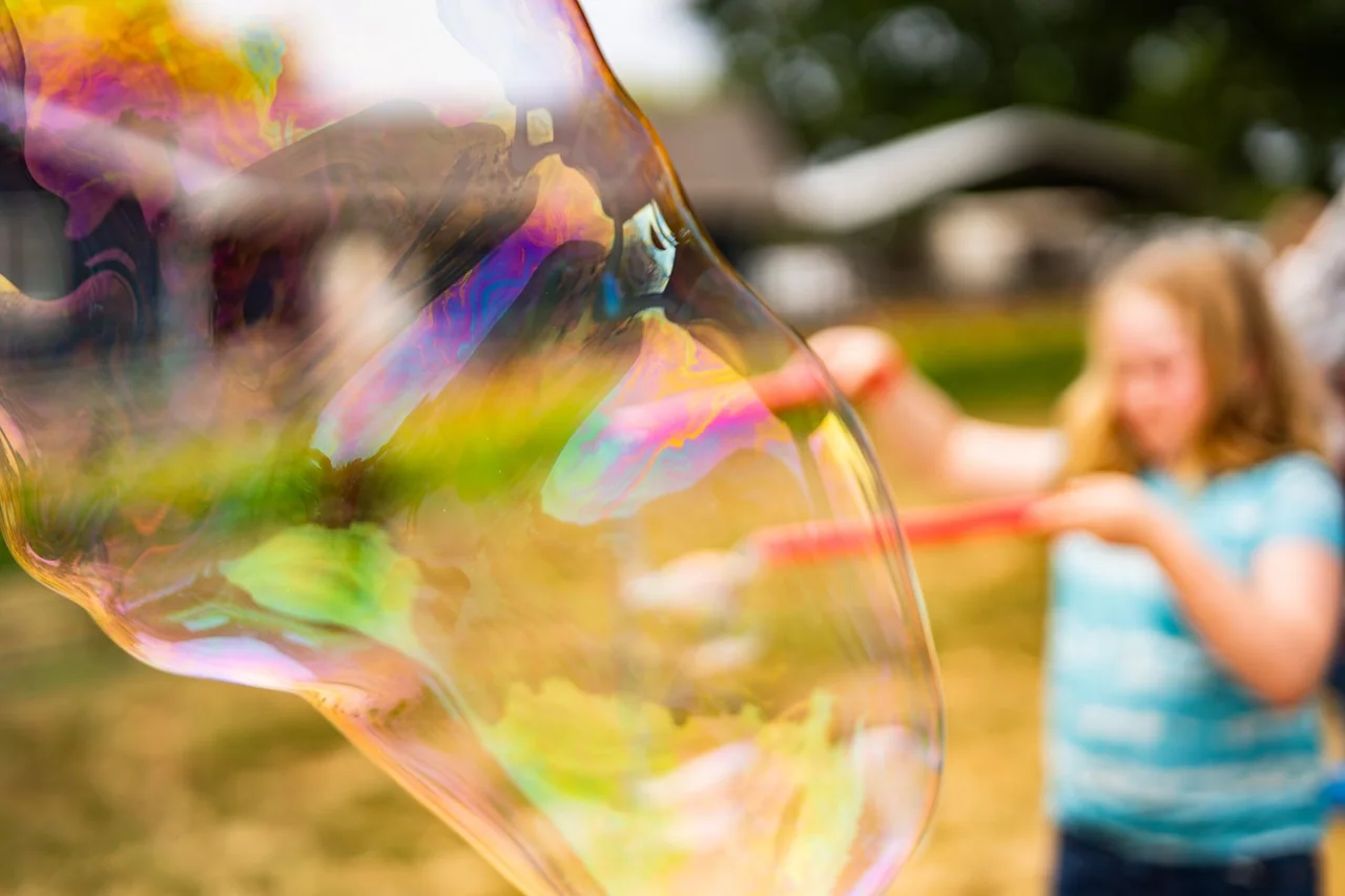 A child seen through an iridescent soap bubble, with the bubble filling most of the foreground.